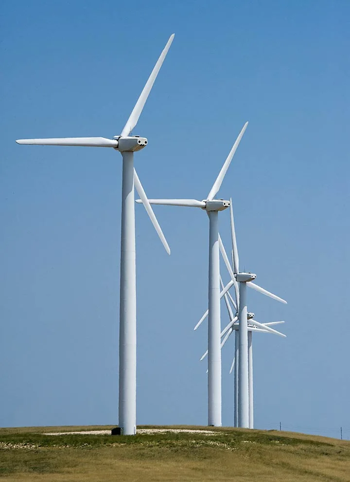 A row of wind turbines beneath a blue sky on the northern Great Plains.