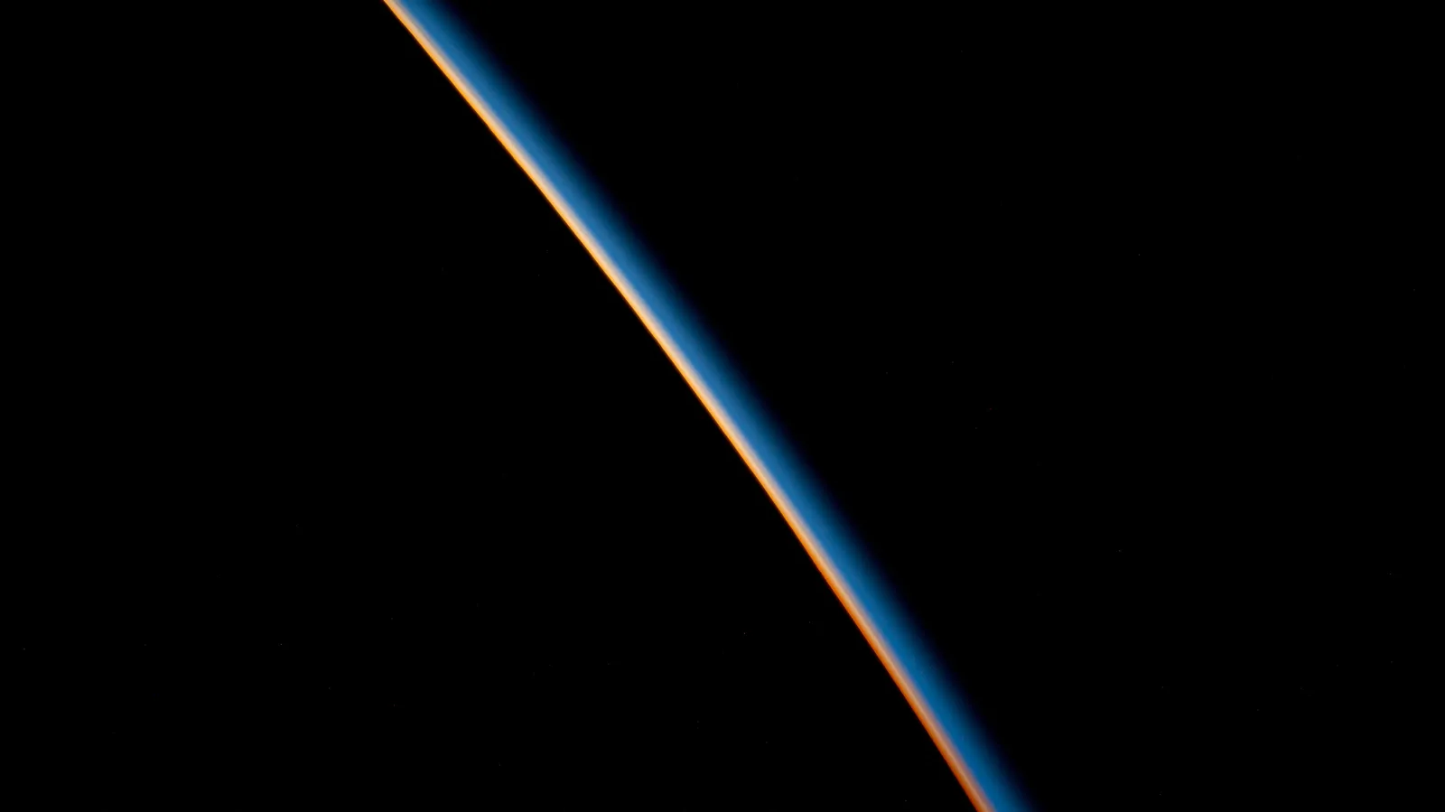 A blue and orange atmospheric glow along the dark edge of Earth, photographed from orbit.